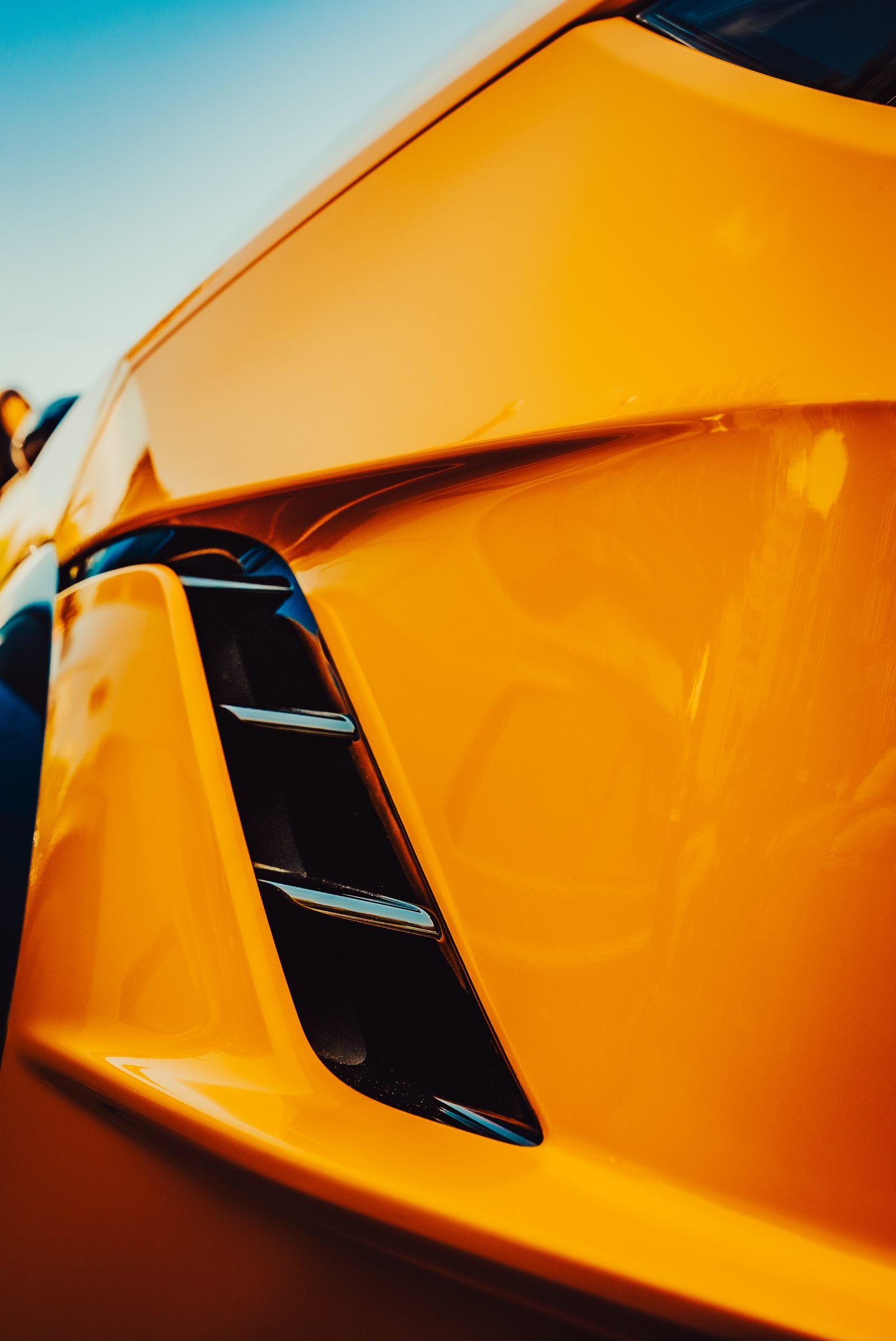 Orange shoulder line of a sports car flowing around a dark vent