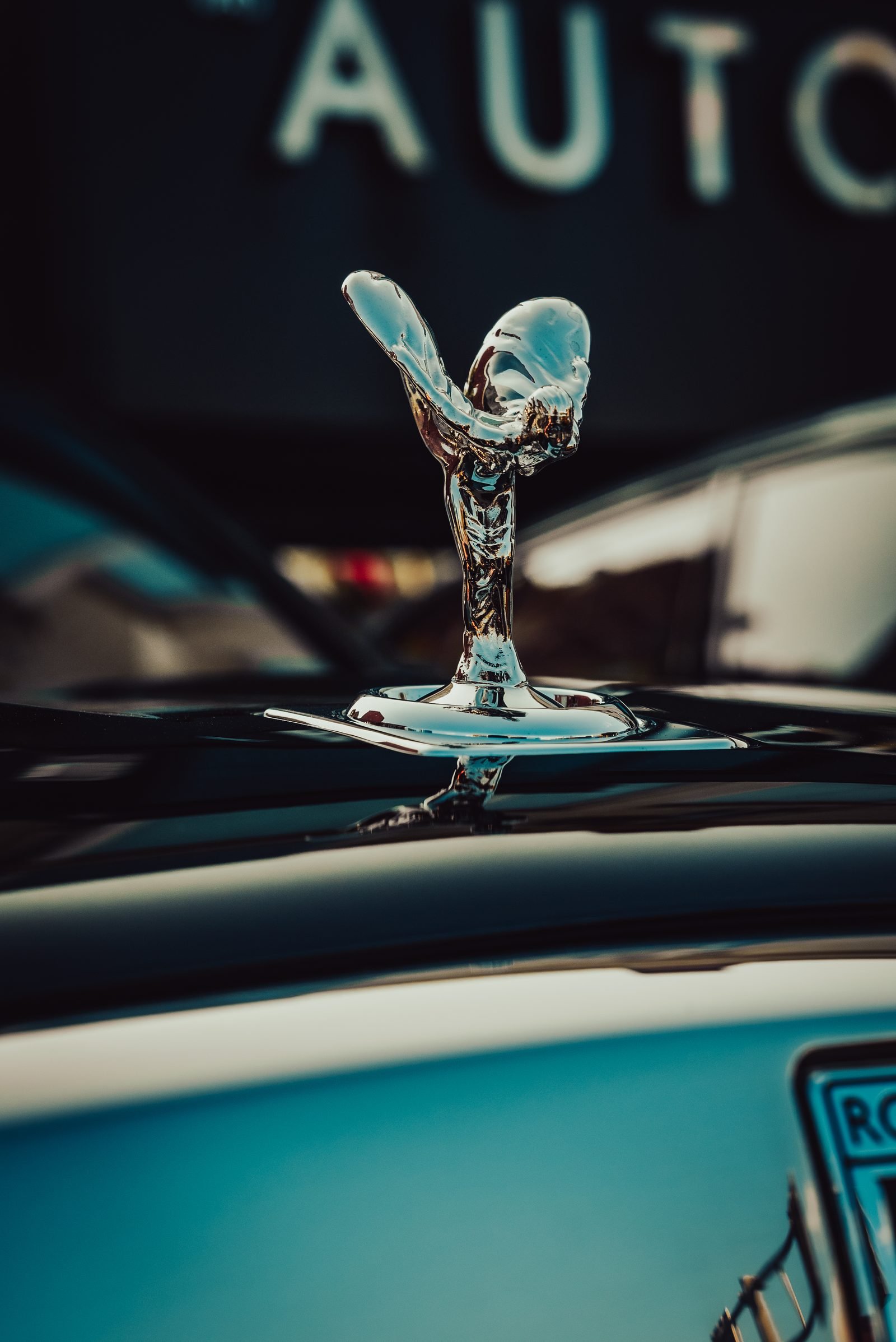 Chrome hood figure with wings swept back, showroom sign soft behind