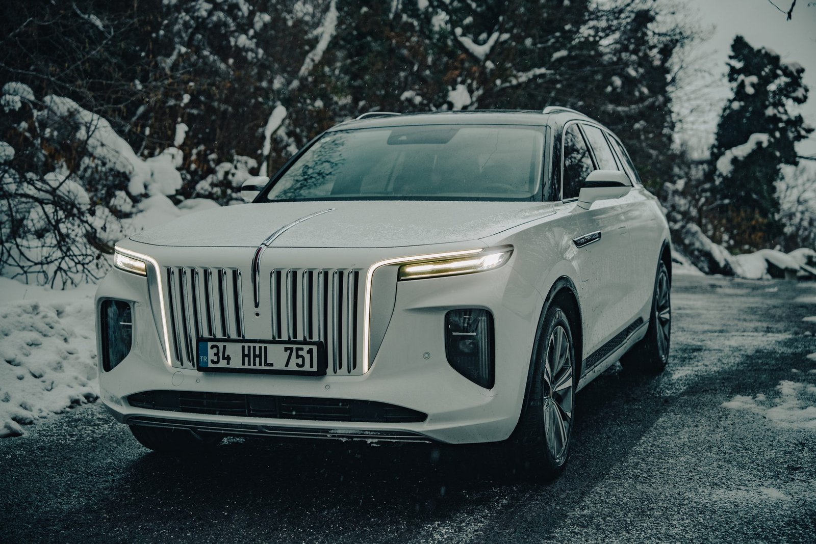 White luxury SUV on a snowy mountain road, snow falling, lamps lit